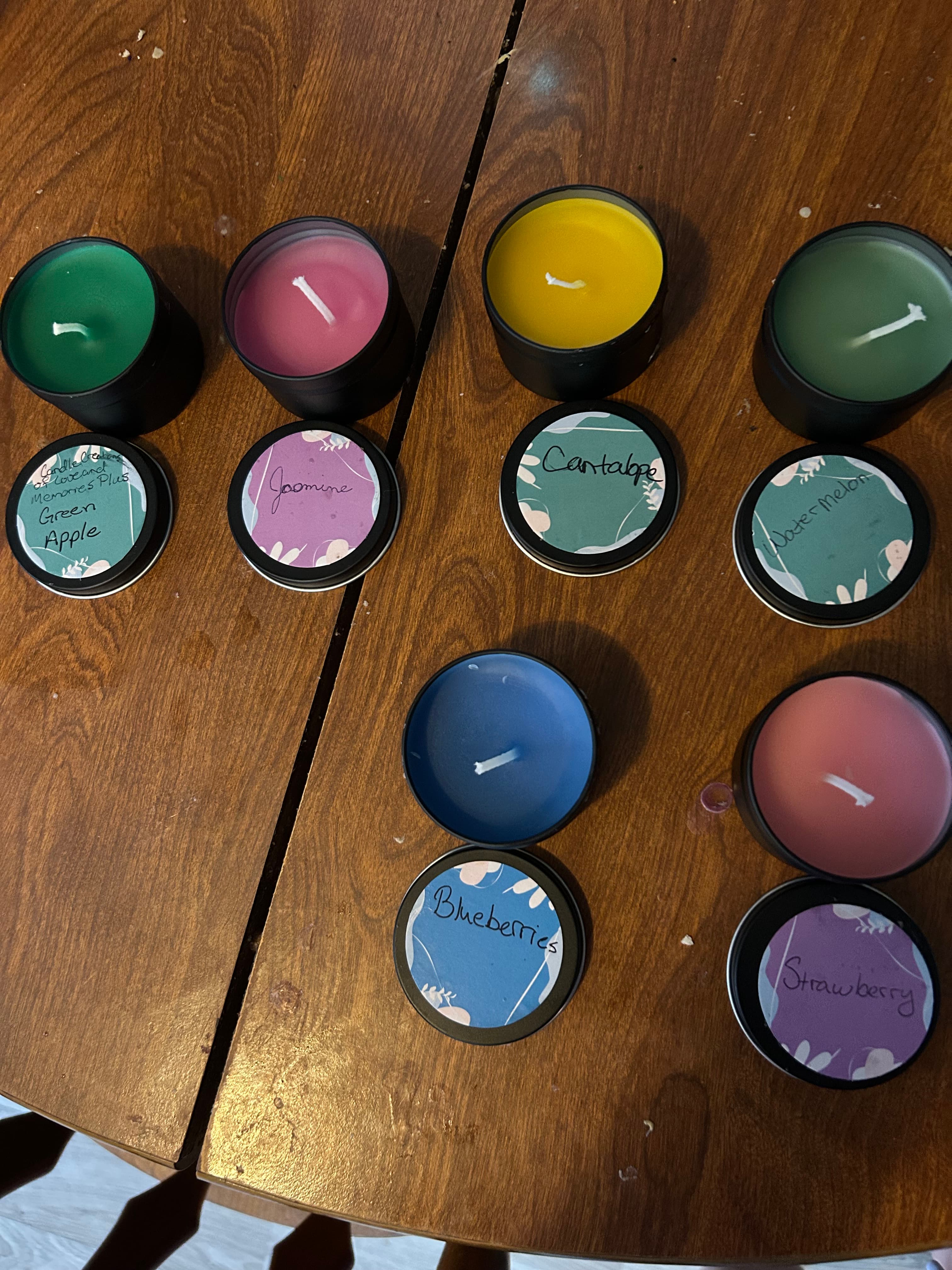 Assorted handmade scented candles with colorful tin lids on wooden table